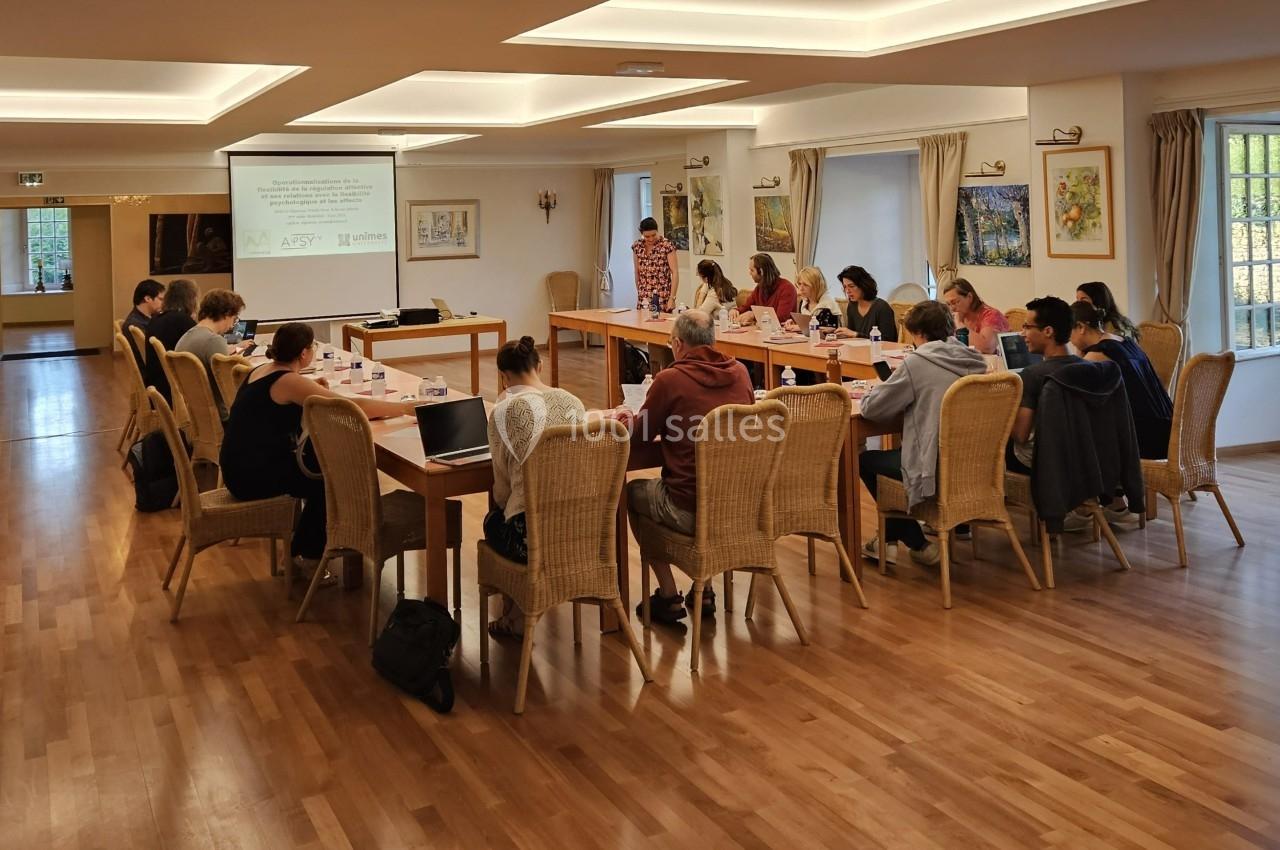 Des personnes assises autour de tables en U dans une salle lumineuse, participant à une réunion ou une formation.
