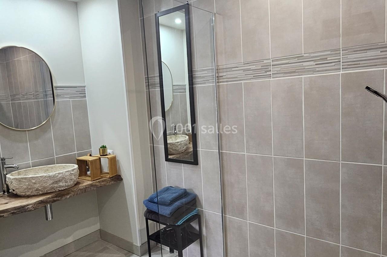 Salle de bain moderne avec douche à l'italienne, lavabo en pierre, miroir rond et éclairage encastré.