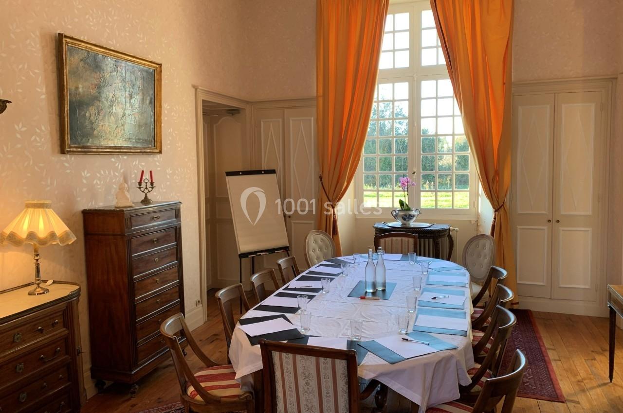 Salle de réunion lumineuse avec table dressée, chaises en bois, chevalet de conférence et grandes fenêtres avec rideaux…