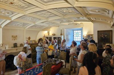 Des personnes en costumes d'époque discutent dans la cour d'un château historique sous un ciel partiellement nuageux.