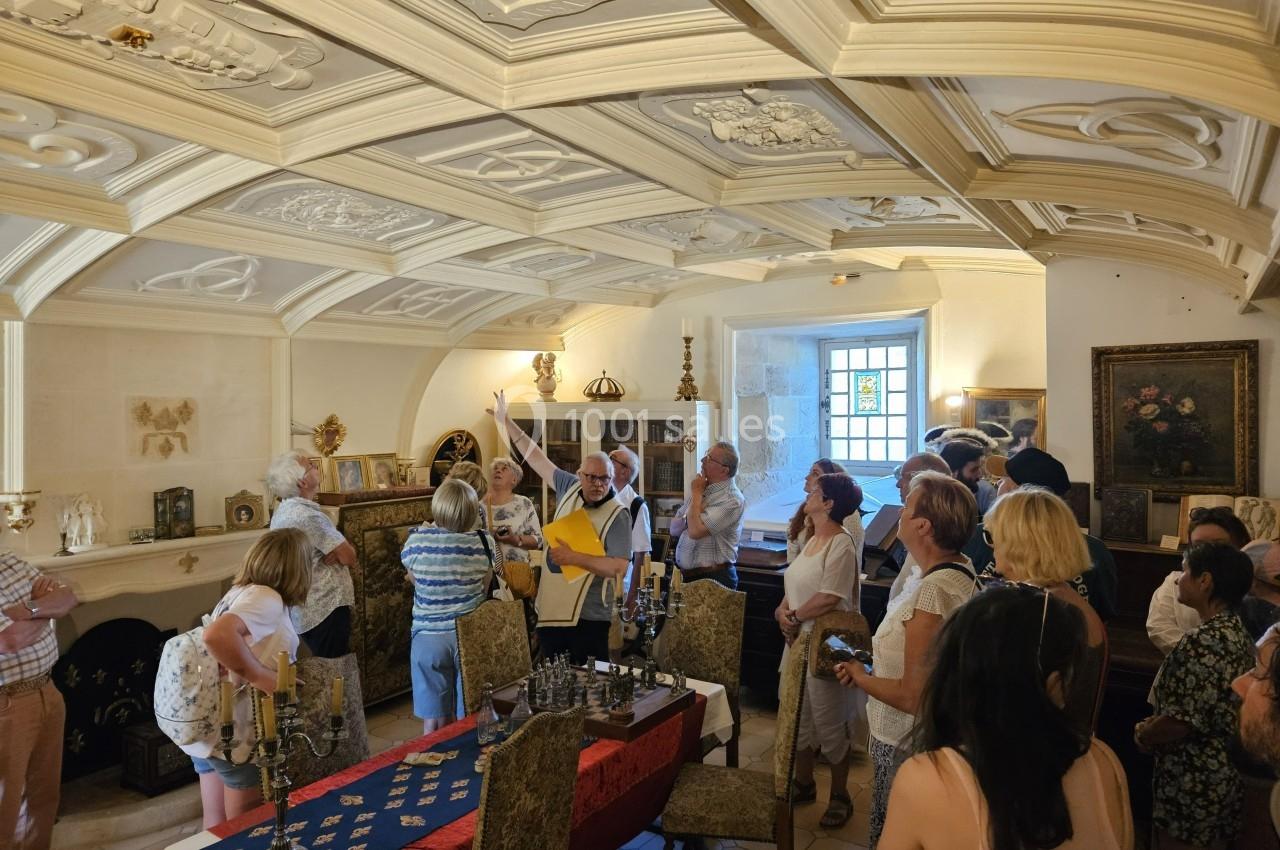 Groupe de personnes écoutant un guide dans une salle au plafond voûté orné, avec des objets anciens exposés.