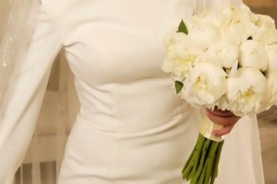 Une mariée en tailleur blanc tenant un bouquet devant une vitrine avec l'inscription ’Love Curated’.
