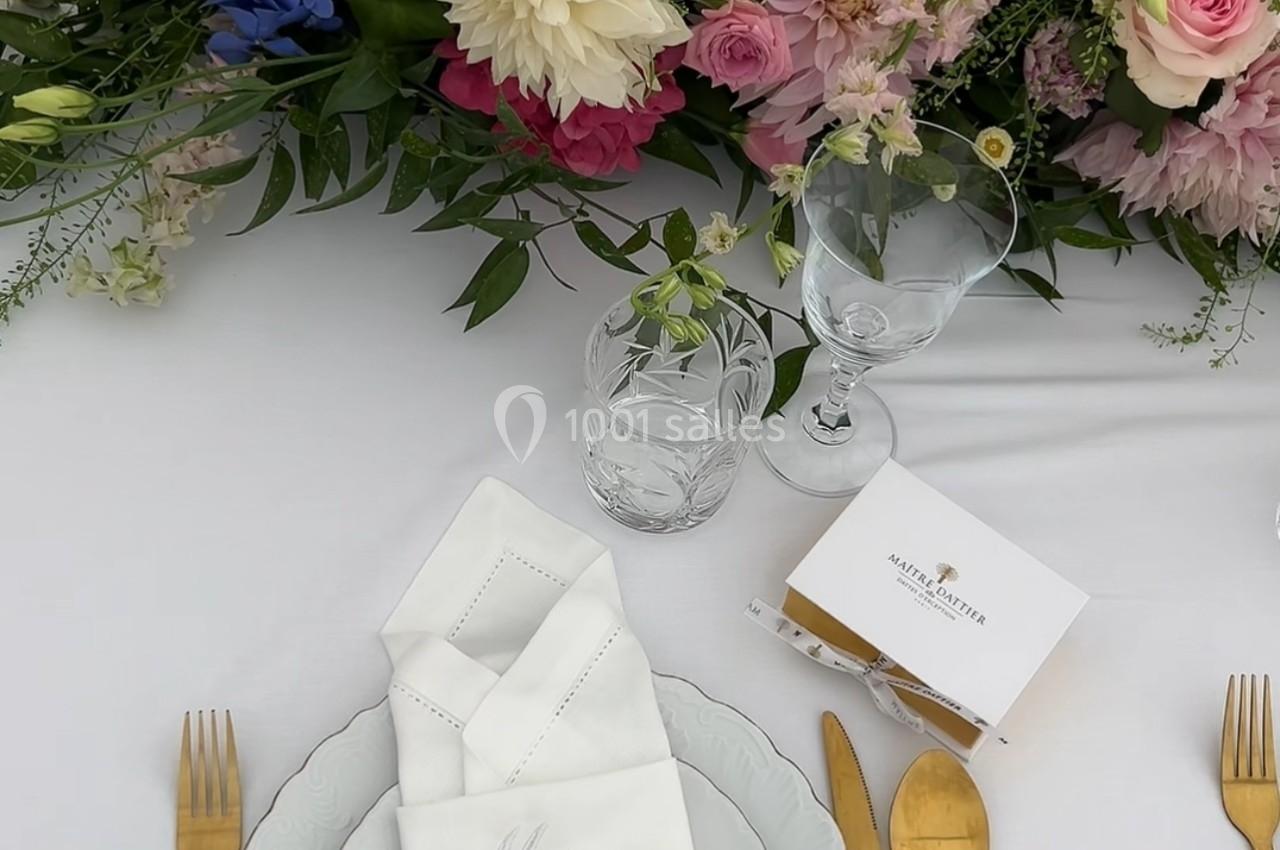 Table dressée avec vaisselle blanche, couverts dorés, serviette pliée et centre de table fleuri aux tons pastel.