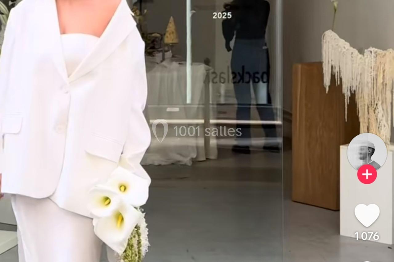 Une mariée en tailleur blanc tenant un bouquet devant une vitrine avec l'inscription ’Love Curated’.