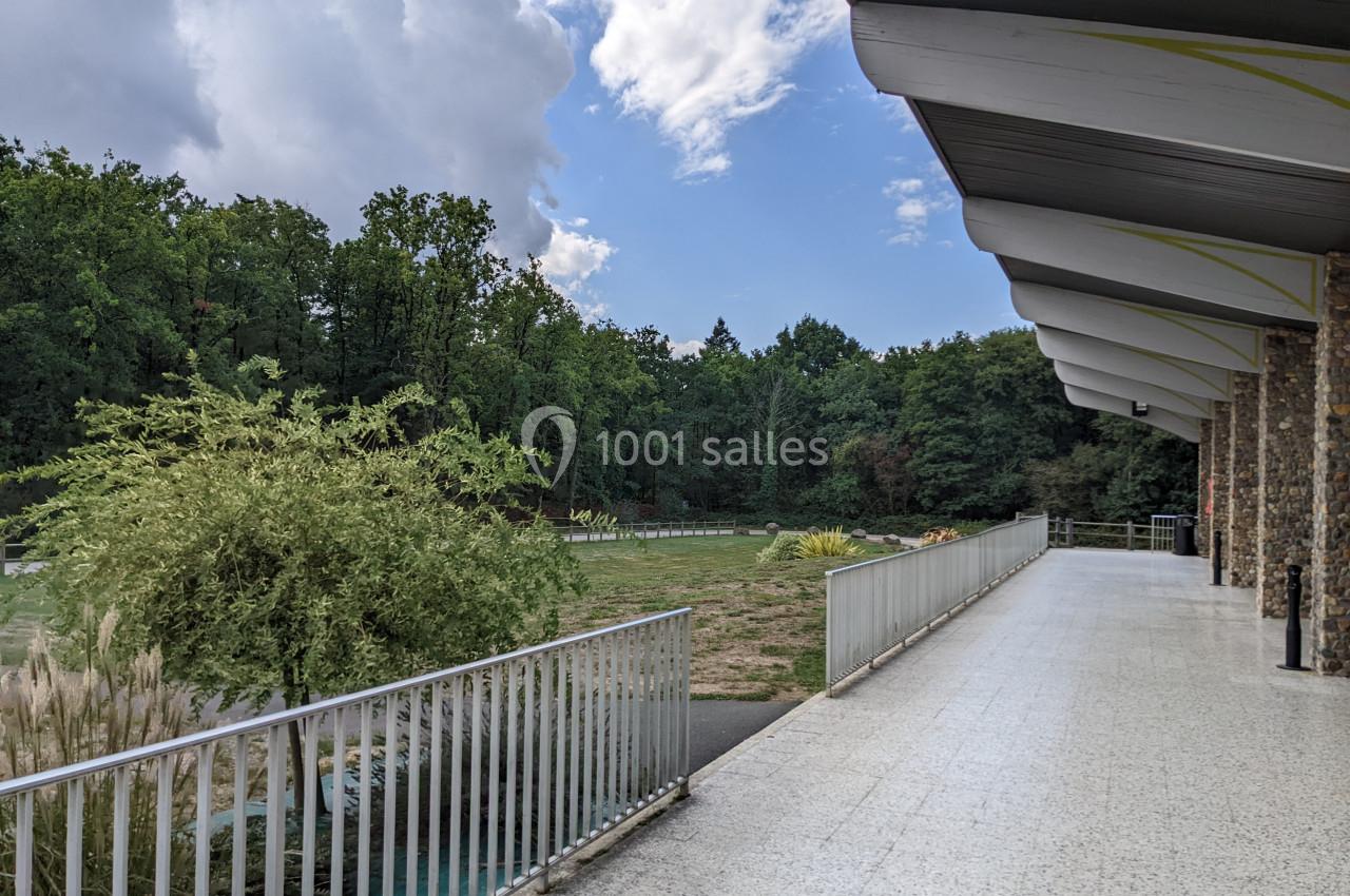 Terrasse couverte avec garde-corps donnant sur un espace vert arboré sous un ciel partiellement nuageux.