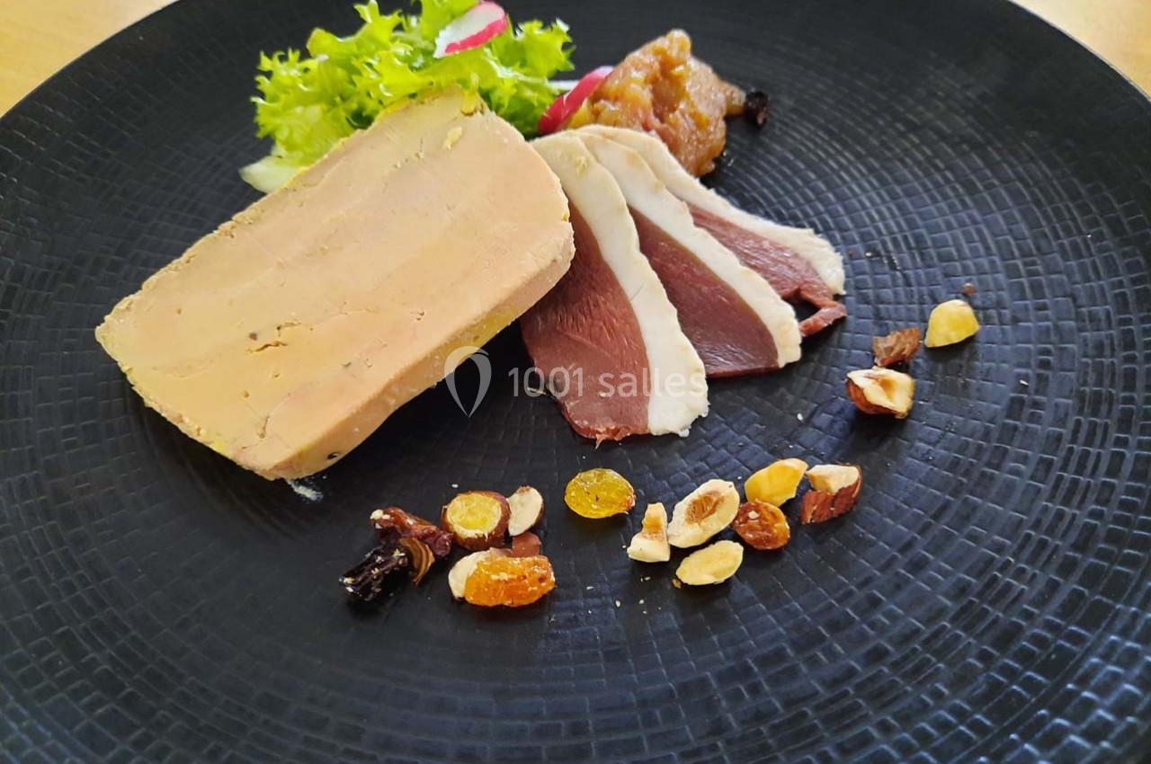 Assiette composée de foie gras, magret de canard fumé, fruits secs, chutney et salade verte sur une assiette noire.