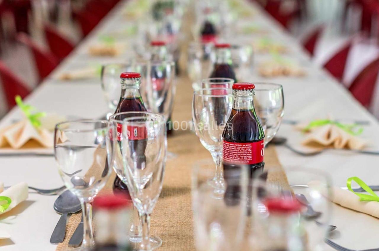 Table dressée avec des verres, bouteilles de soda et serviettes pliées, décorée d’un chemin de table en toile de jute.