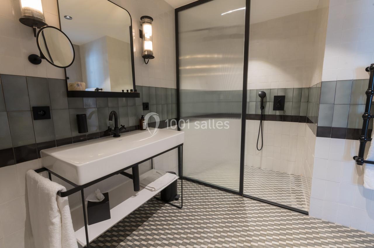 Salle de bain moderne avec douche à paroi vitrée, lavabo sur meuble noir et carrelage géométrique au sol.