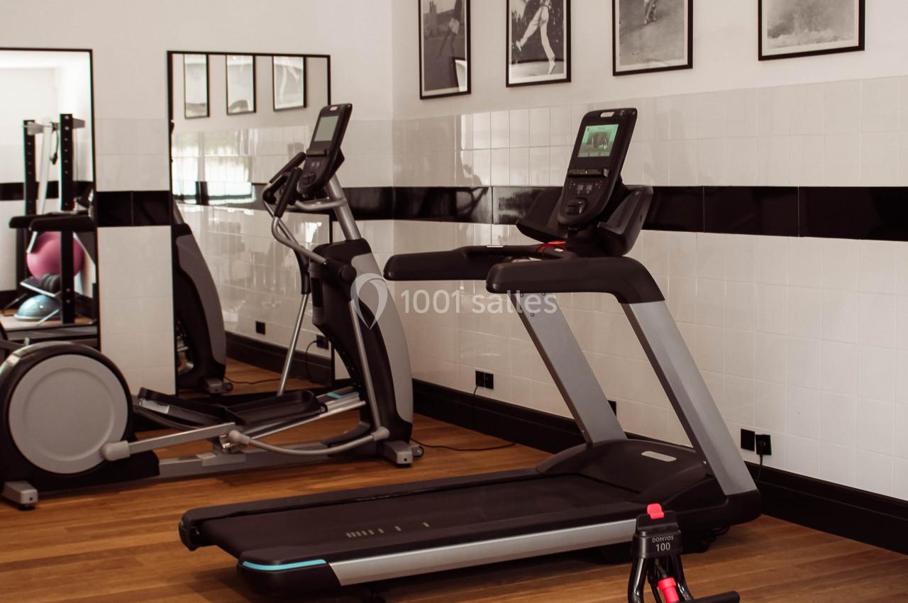 Salle de sport avec tapis de course, vélo elliptique, rameur et décorations murales en noir et blanc.