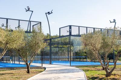 Terrains de padel extérieurs entourés d'arbres et éclairés par des lampadaires, avec un chemin en premier plan.