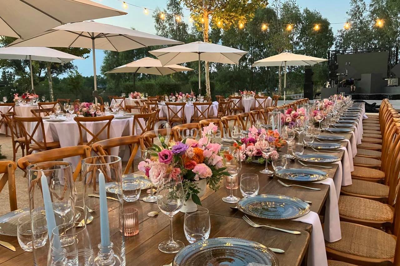Tables décorées avec des fleurs colorées et des chandeliers, disposées en extérieur sous des guirlandes lumineuses.