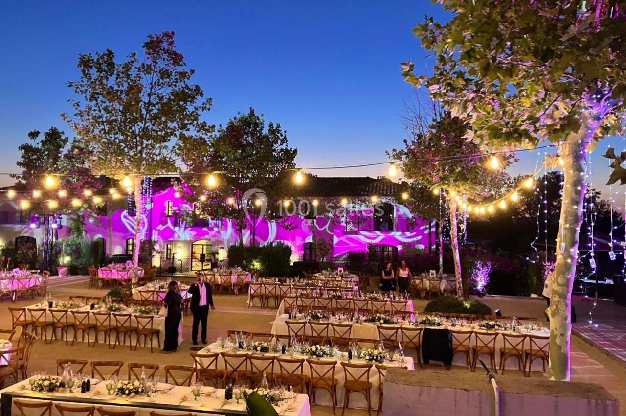 Terrasse décorée pour un événement en soirée, avec guirlandes lumineuses, tables dressées et éclairages colorés.