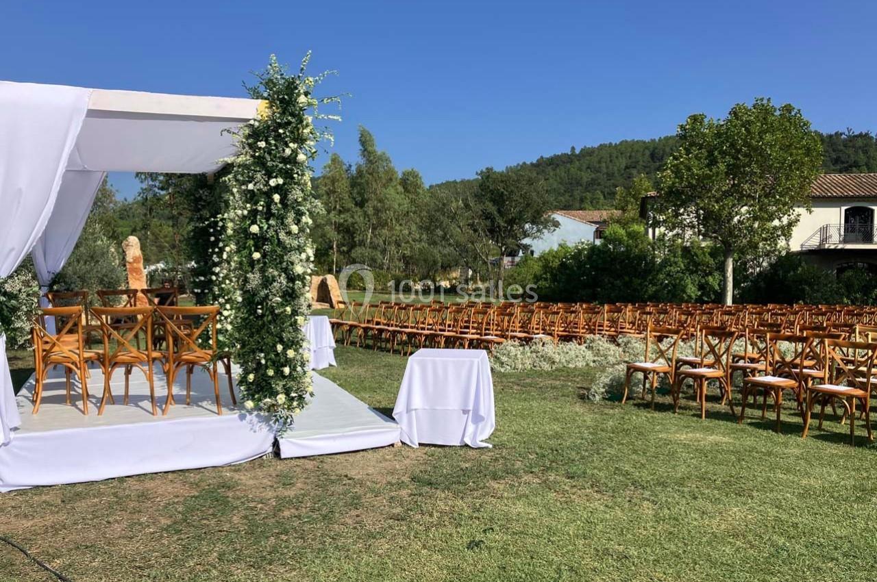 Cérémonie de mariage en plein air avec une arche fleurie, des chaises en bois et un paysage verdoyant en arrière-plan.