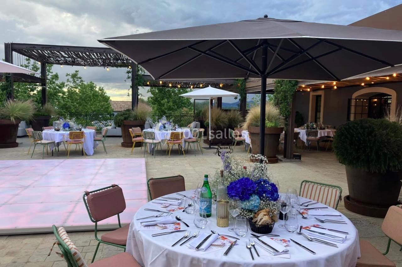 Terrasse aménagée pour un événement avec tables dressées, parasols, piste de danse et décorations florales.