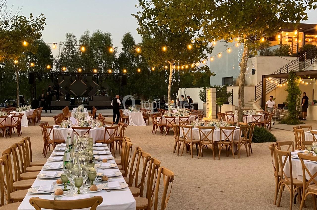 Tables dressées en extérieur pour un événement, entourées de guirlandes lumineuses et de végétation au crépuscule.