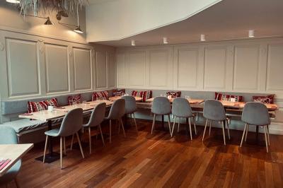 Banquette grise avec coussins rouges à motifs, tables en bois dressées, décor mural avec luminaires et ornements végétaux.