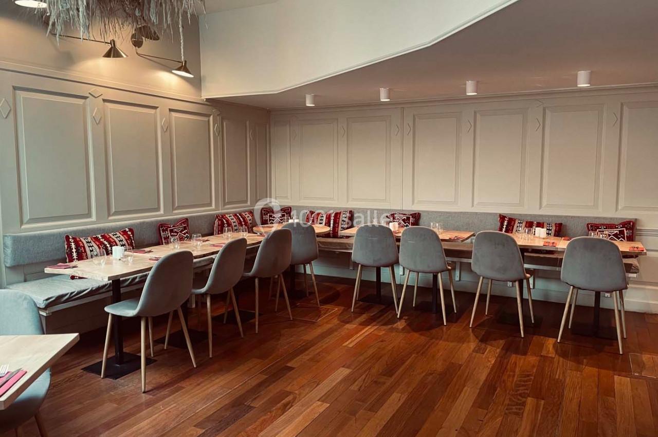 Salle de restaurant avec tables en bois, chaises grises et banquettes décorées de coussins à motifs rouges.