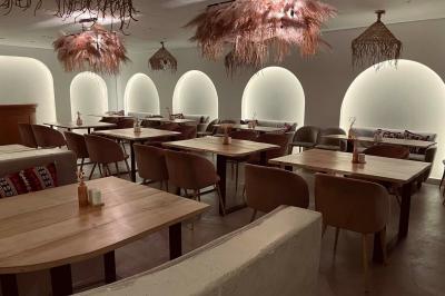 Banquette grise avec coussins rouges à motifs, tables en bois dressées, décor mural avec luminaires et ornements végétaux.