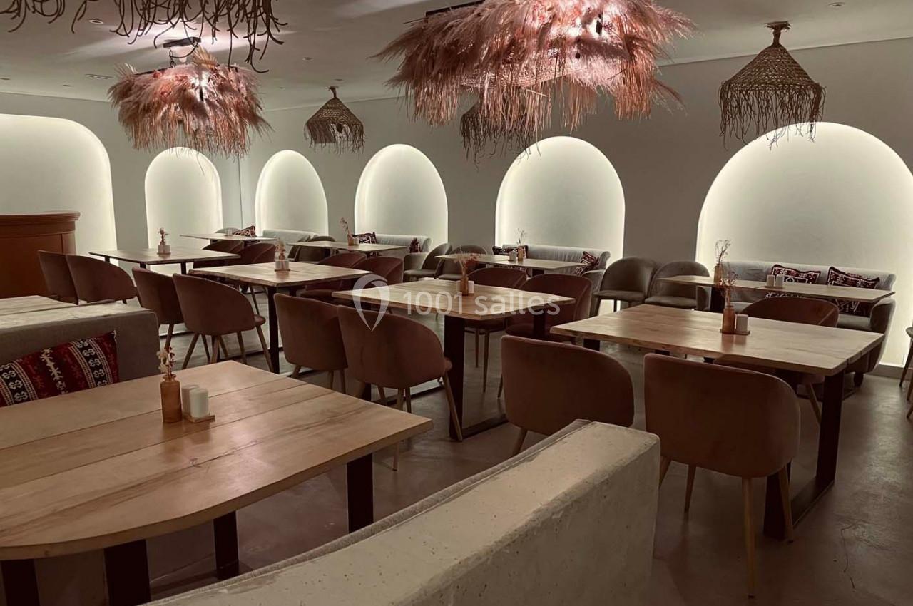 Salle de restaurant moderne avec tables en bois, chaises rembourrées et luminaires décoratifs suspendus.