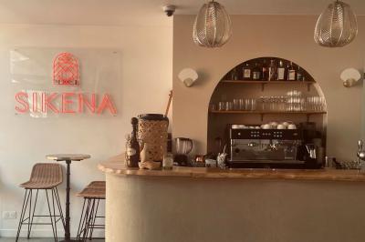 Banquette grise avec coussins rouges à motifs, tables en bois dressées, décor mural avec luminaires et ornements végétaux.