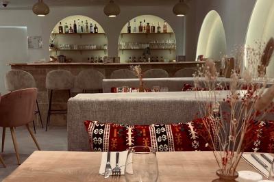 Banquette grise avec coussins rouges à motifs, tables en bois dressées, décor mural avec luminaires et ornements végétaux.