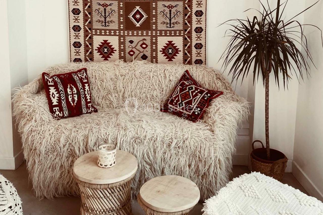 Canapé recouvert de tissu duveteux, coussins à motifs ethniques, tapis mural assorti et table basse en bois clair.