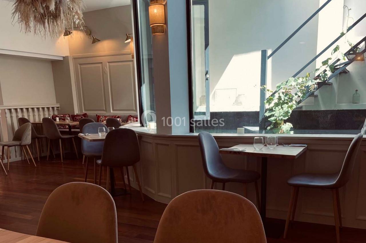 Salle de restaurant lumineuse avec tables en bois, chaises modernes et escalier vitré en arrière-plan.