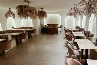 Banquette grise avec coussins rouges à motifs, tables en bois dressées, décor mural avec luminaires et ornements végétaux.