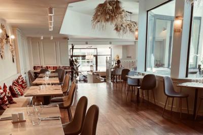 Banquette grise avec coussins rouges à motifs, tables en bois dressées, décor mural avec luminaires et ornements végétaux.