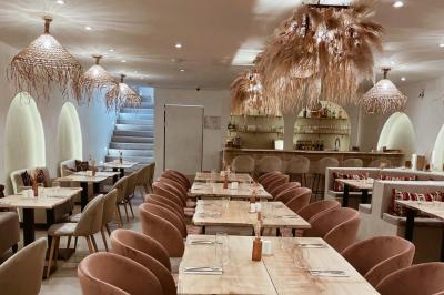 Banquette grise avec coussins rouges à motifs, tables en bois dressées, décor mural avec luminaires et ornements végétaux.