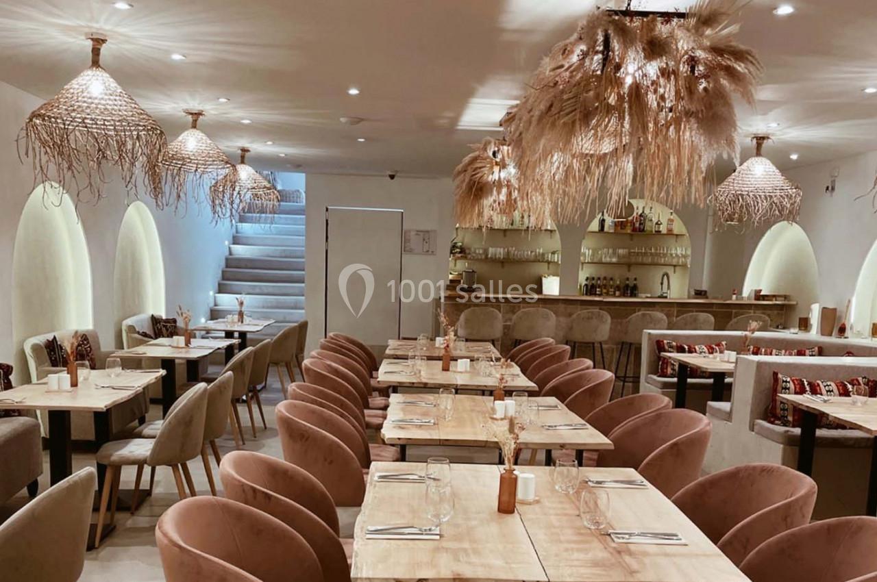 Salle de restaurant lumineuse avec tables en bois, chaises rembourrées et décorations suspendues en fibres naturelles.