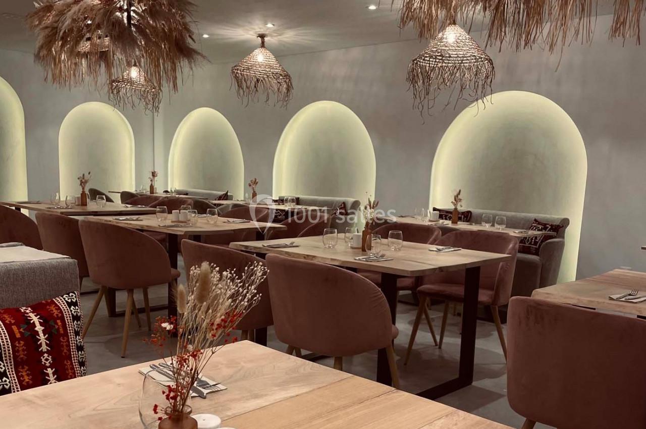Salle de restaurant avec tables en bois, chaises rembourrées, arches lumineuses et décorations en fibres naturelles.