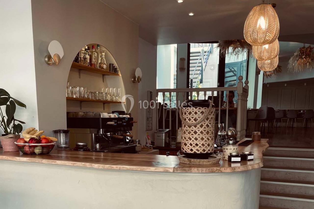 Comptoir de café avec machine à expresso, paniers décoratifs, fruits et étagères contenant des bouteilles et des verres.