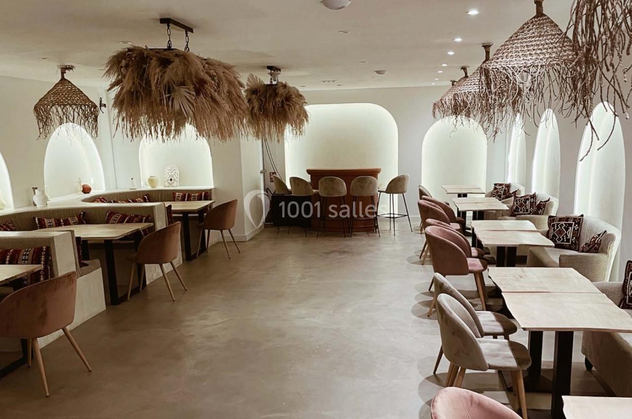 Salle de restaurant lumineuse avec tables en bois, chaises rembourrées et décorations suspendues en fibres naturelles.