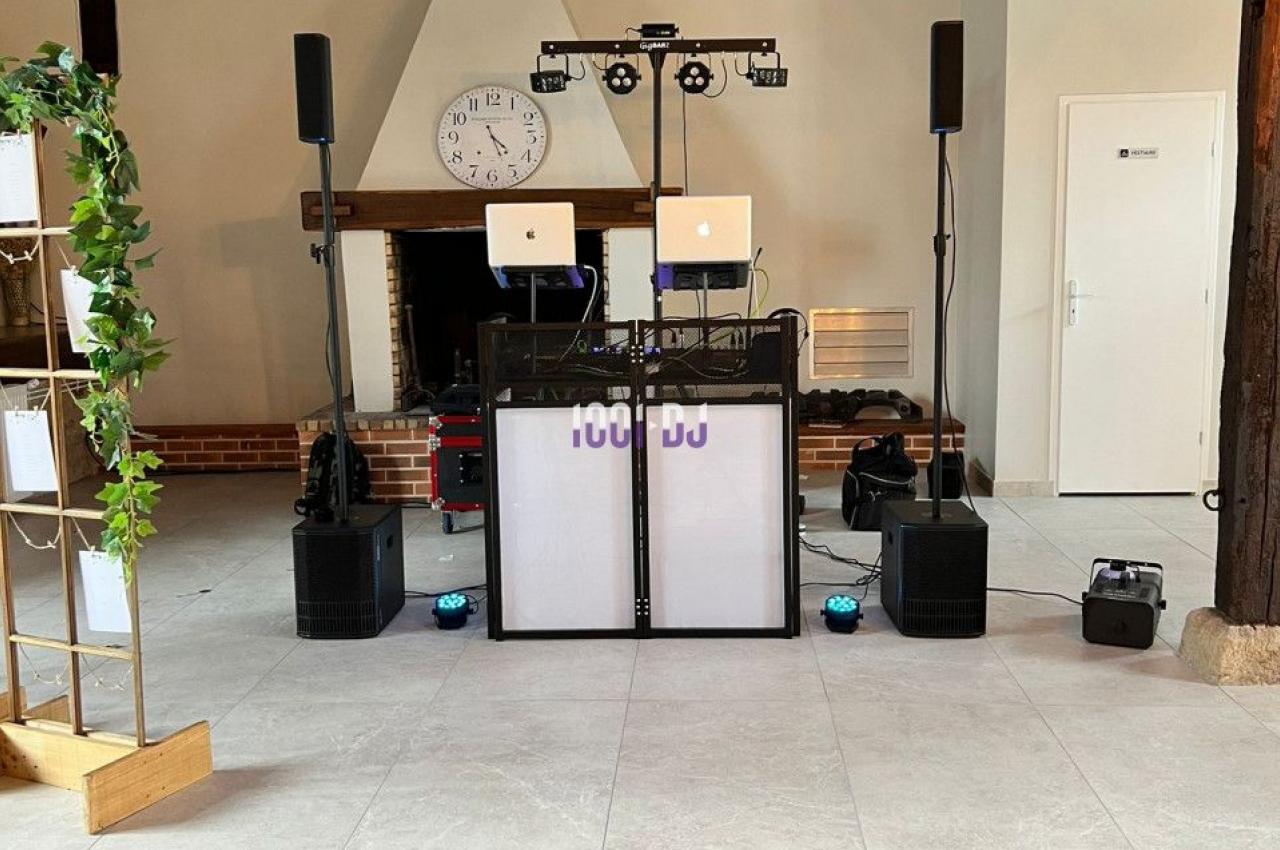 Installation de matériel de DJ avec enceintes, lumières et ordinateurs dans une salle avec poutres apparentes et cheminée.