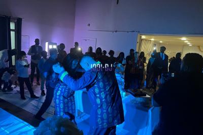 Un DJ souriant derrière une table équipée de matériel audio, avec un ordinateur portable et une table de mixage.