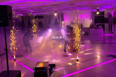 Un DJ souriant derrière une table équipée de matériel audio, avec un ordinateur portable et une table de mixage.