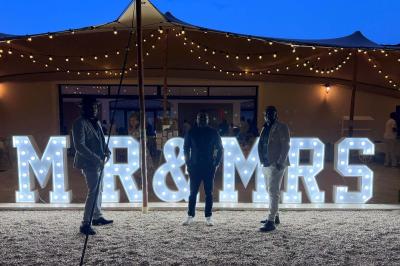 Un DJ souriant derrière une table équipée de matériel audio, avec un ordinateur portable et une table de mixage.