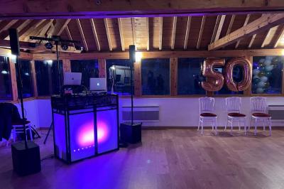 Un DJ souriant derrière une table équipée de matériel audio, avec un ordinateur portable et une table de mixage.