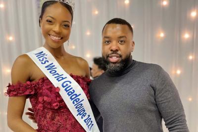Un DJ souriant derrière une table équipée de matériel audio, avec un ordinateur portable et une table de mixage.