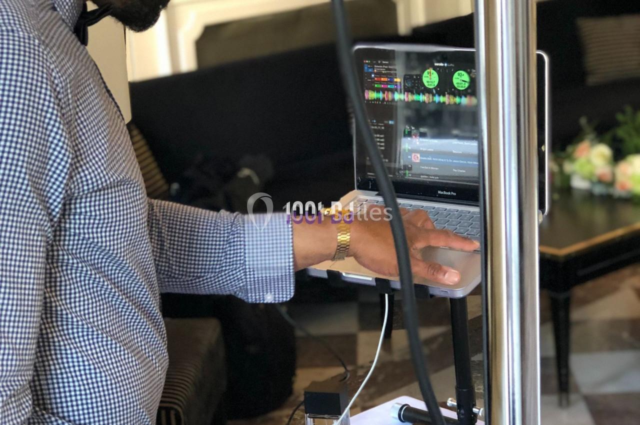 Un DJ ajuste les réglages sur une table de mixage connectée à un ordinateur lors d'un événement en intérieur.