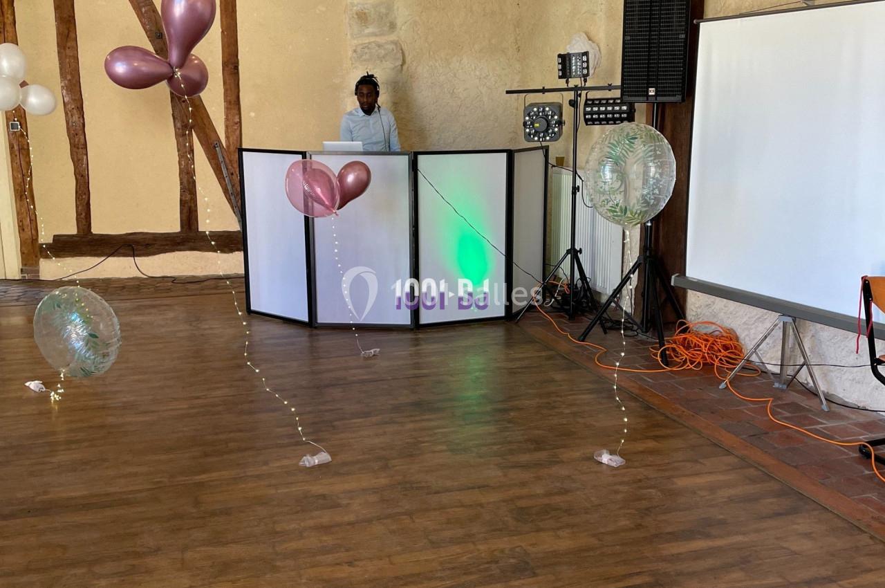 Salle de réception avec parquet, décorations de ballons, éclairage, et un DJ derrière une table lumineuse.