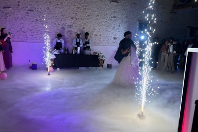 Des personnes dansent dans une salle en pierre éclairée par des lumières colorées, créant une ambiance festive.