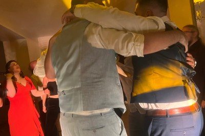 Des personnes dansent dans une salle en pierre éclairée par des lumières colorées, créant une ambiance festive.