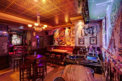 Salle animée avec des personnes dansant sous des lumières colorées, décorée de plantes suspendues et de graffitis.