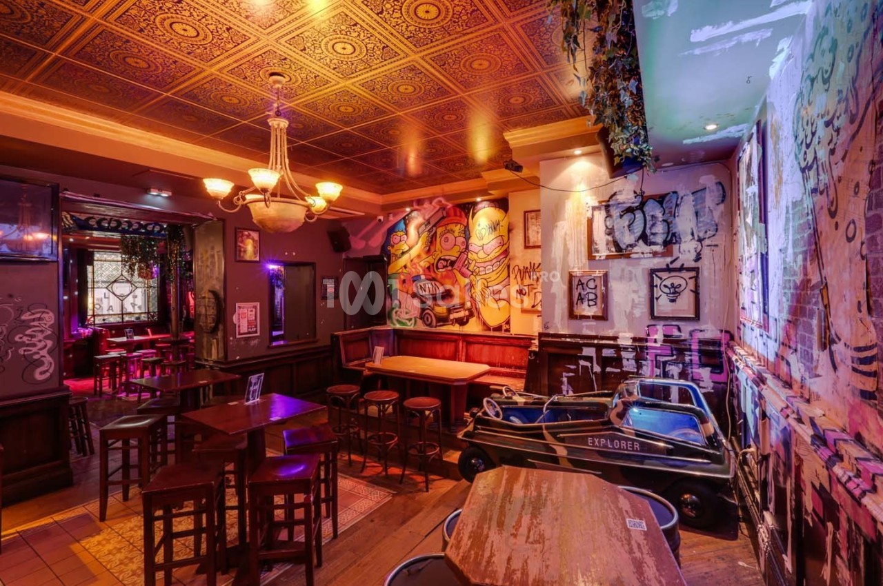 Intérieur d'un bar avec des murs décorés de graffitis, des tables en bois et un plafond orné de motifs dorés.