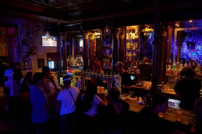 Salle animée avec des personnes dansant sous des lumières colorées, décorée de plantes suspendues et de graffitis.