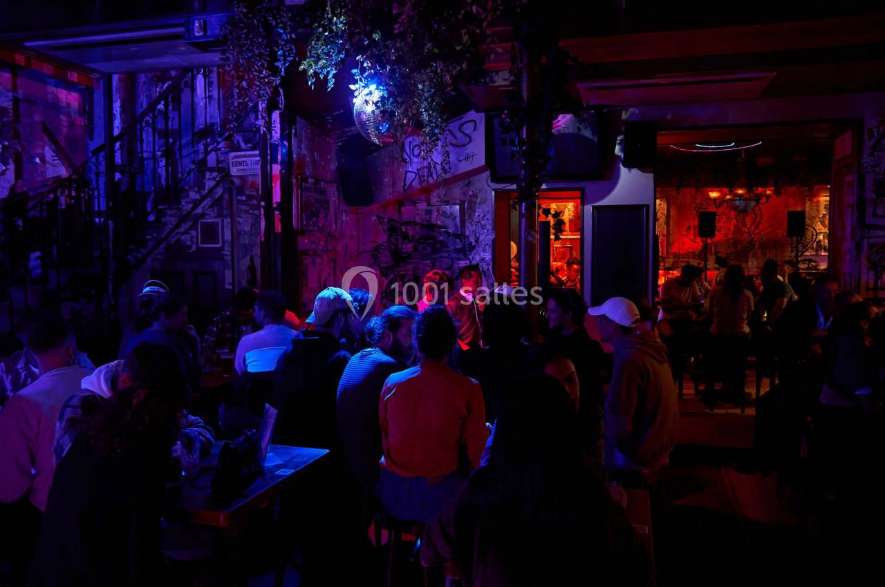 Groupe de personnes assises dans un bar à l'ambiance tamisée avec des lumières colorées et un décor urbain.
