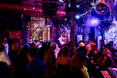 Salle animée avec des personnes dansant sous des lumières colorées, décorée de plantes suspendues et de graffitis.