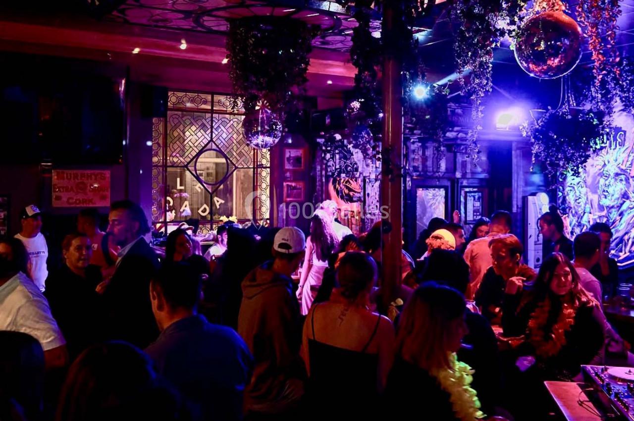 Groupe de personnes dans un bar animé avec éclairage coloré, décorations suspendues et ambiance festive.